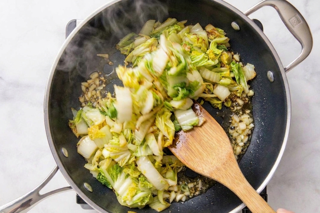 Napa cabbage stir-fry being tossed in a skillet with a wooden spatula over a stovetop