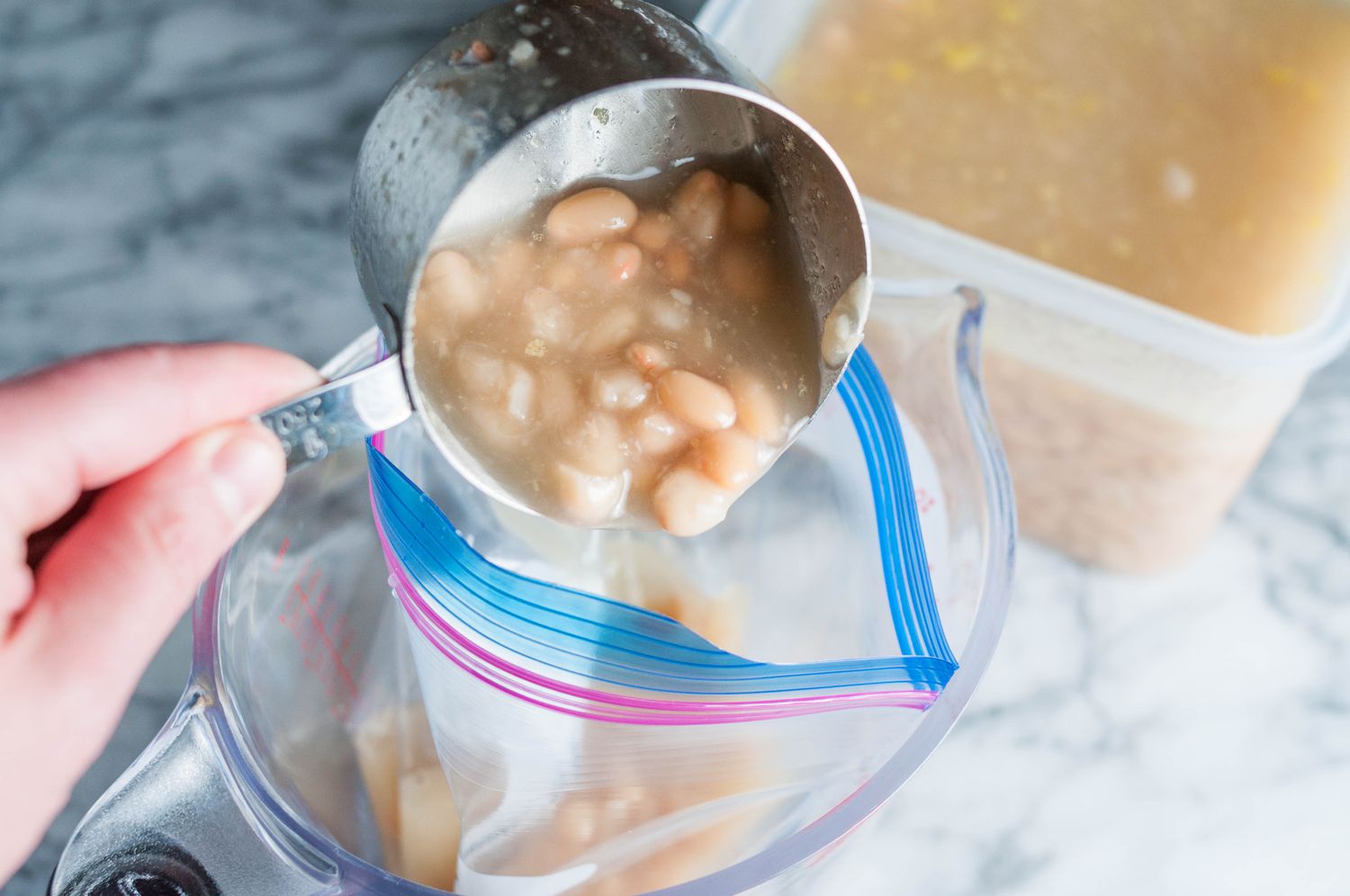 Several freezer-safe soup portions in clear containers and silicone trays on a kitchen counter with a ladle nearby