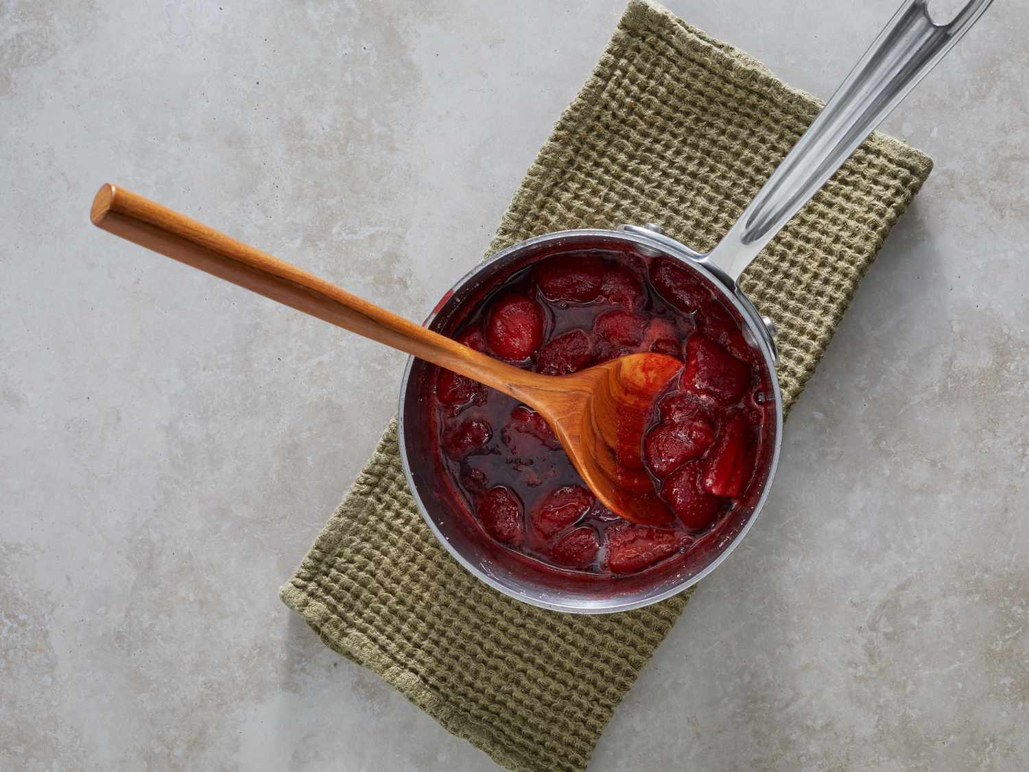 Strawberry sauce simmering in a small saucepan as it thickens into a glossy topping